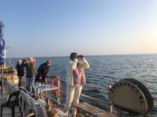 Bezoekers kijken met een verrekijker over de Oosterschelde tijdens de boottocht